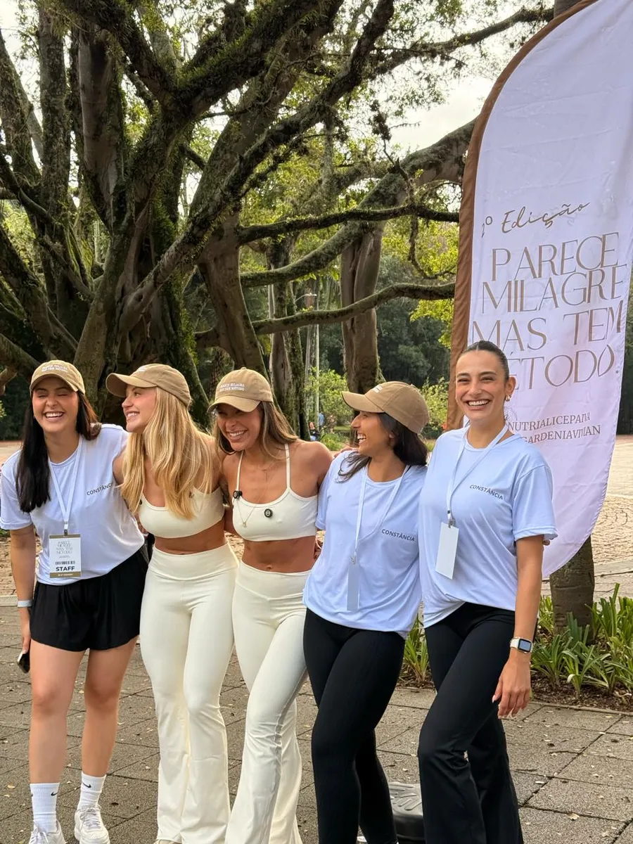 Grupo de participantes sorrindo ao lado da bandeira do evento no parque